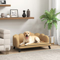 Dog sitting on a small beige sofa in a living room with a plant and shelves in the background.